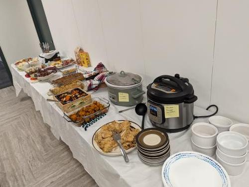 A long table with various casserole dishes, bowls, and two croc pots. George brought John Owen's traditional soup, and other highlights included chicken, sweet potatoes, rosemary bread, and meat and cheese boards.